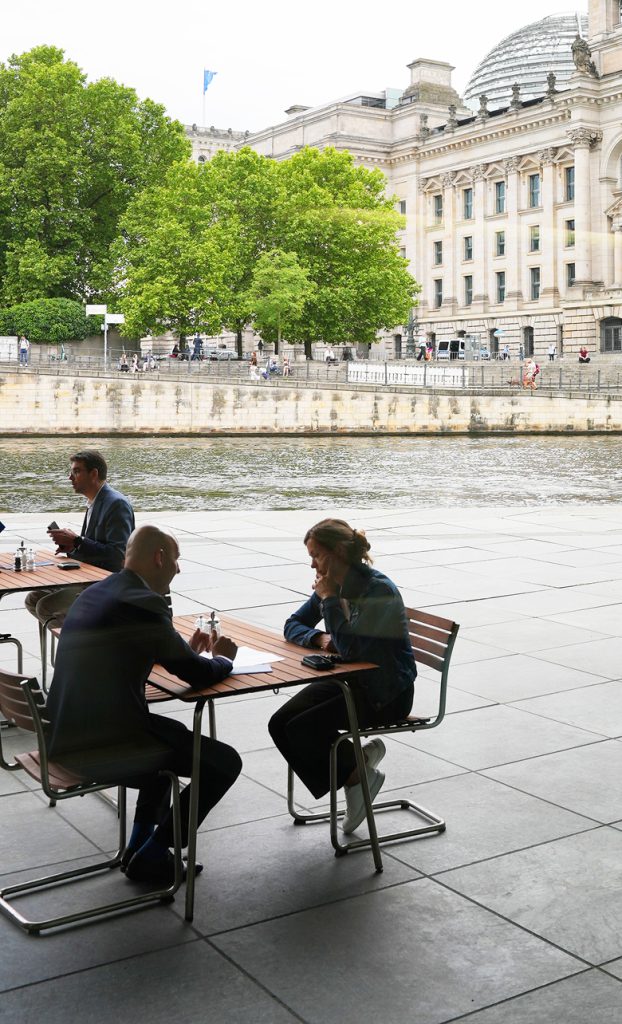 Gäste sitzen an Tischen des Bistro Marie. Im Hintergrund sehen wir die Spree und das Reichstagsgebäude.