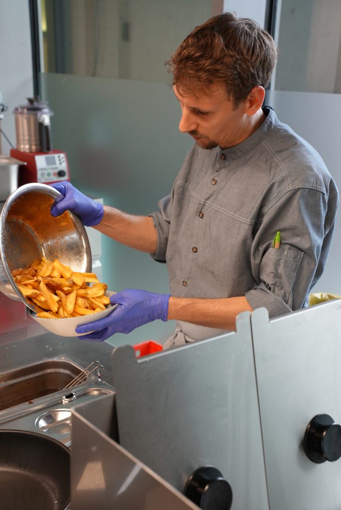 Ein Koch bereitet in der Küche des Bistro Marie leckere Kartoffel-Wedges zu.